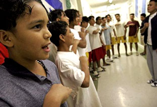 Marion, left, 12, sings the national anthem of Honduras with other children at a Texas shelter.
